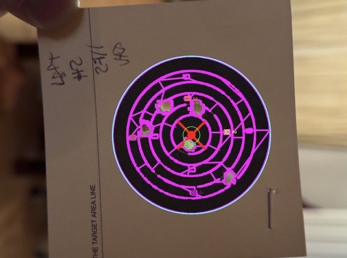 A close-up of a single NSRA bull card with pink computer-vision overlays drawn across every detected feature: the concentric scoring rings, the central aiming cross, the small printed scoring numerals, and the annotation squares at the cardinal points. Actual bullet holes on the card are small and mostly unmarked.