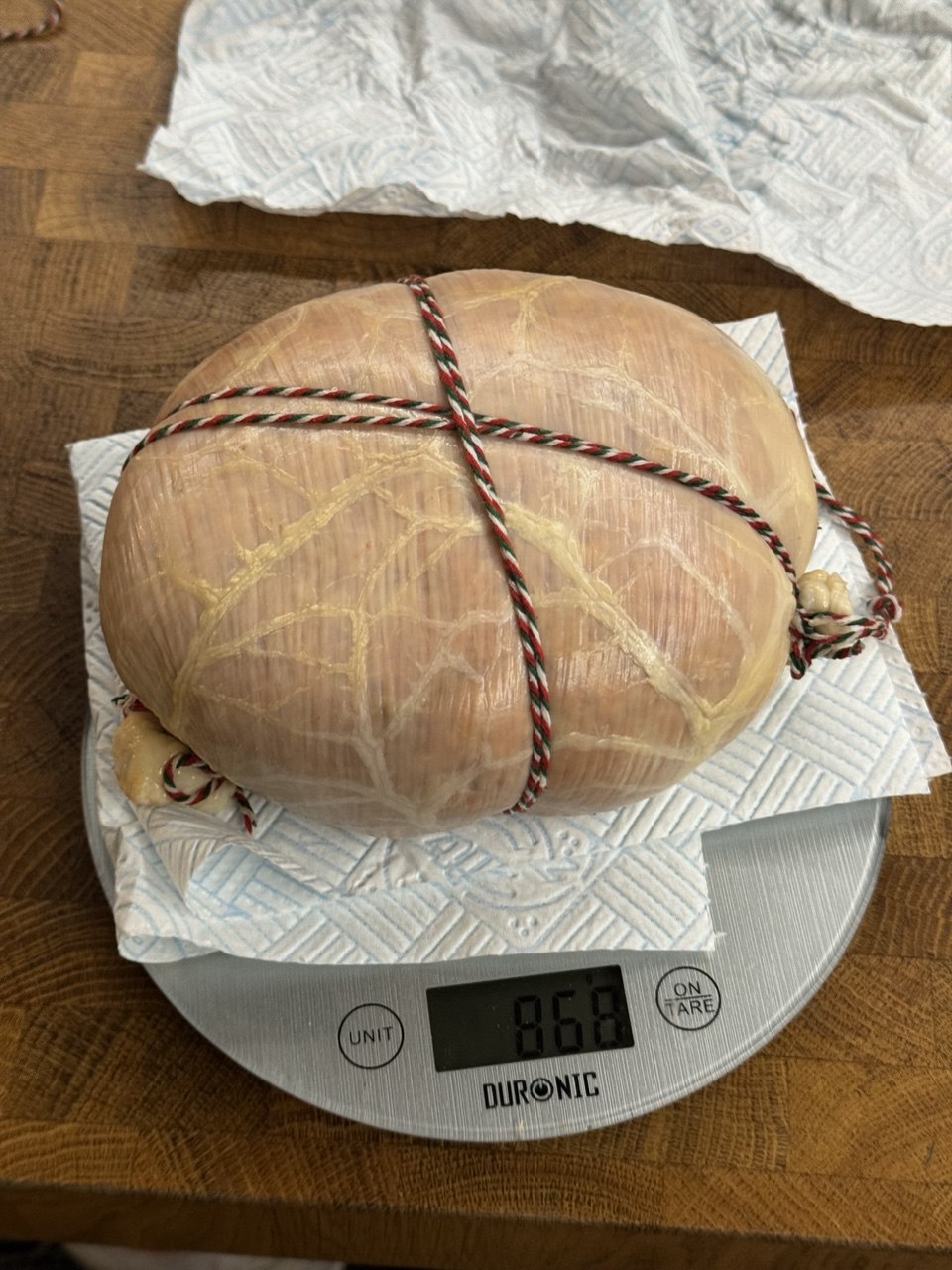 Digital scale on a counter with a salami being weighed.